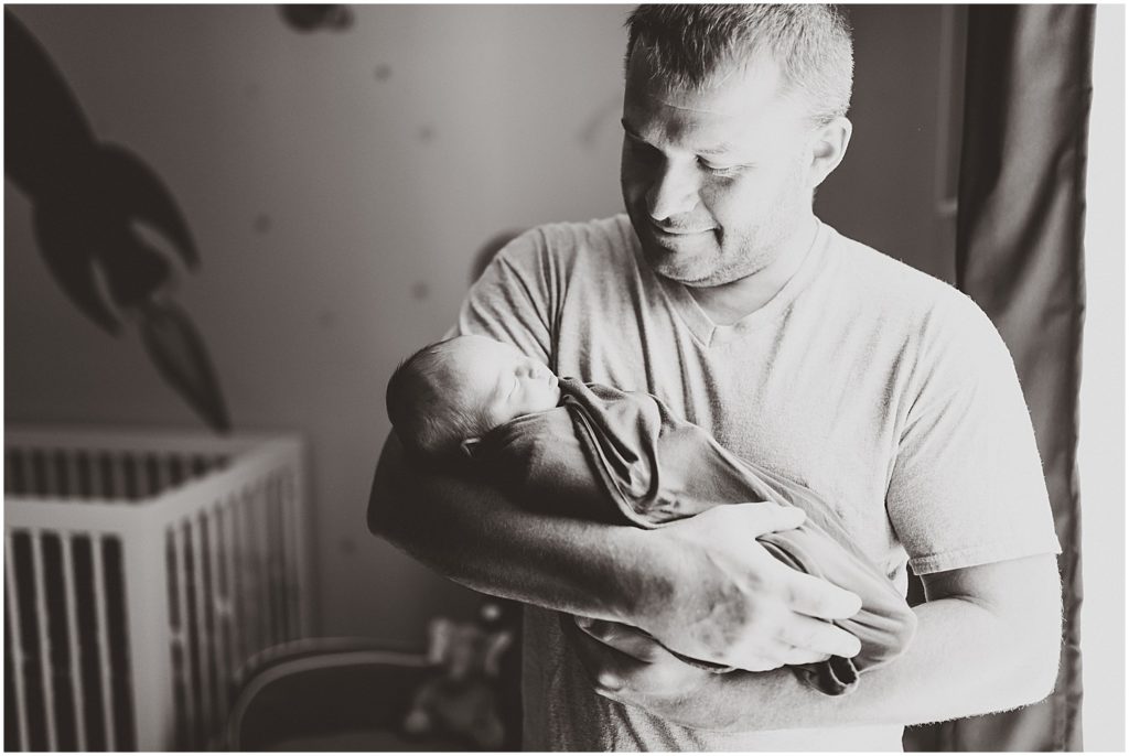 dad in black and white holding newborn by window