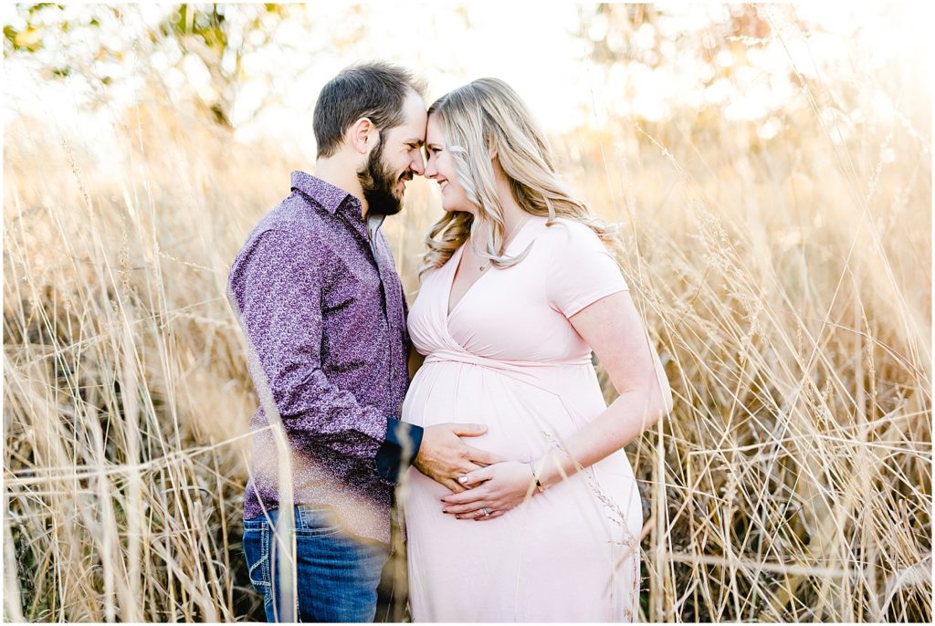 expecting couple standing in tall grasses holding baby belly