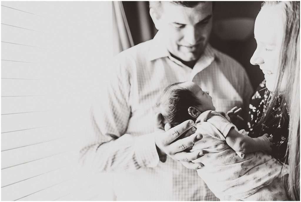 black and white image of parents holding baby boy next to window