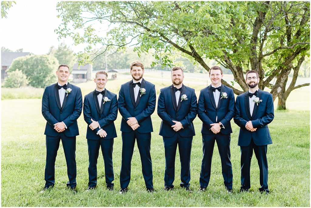 groom and groomsmen line up smiling at camera for wedding party photo