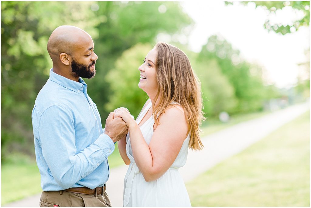 couple holds hands and laughs in sunlight during engagement session at jefferson city greenway trail