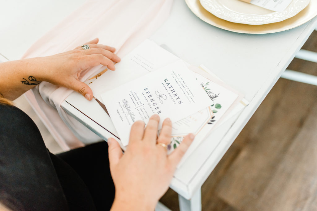 woman sorts through wedding invitation samples at a white table