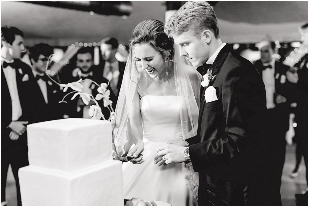 black and white image of bride and groom cutting the cake during wedding reception