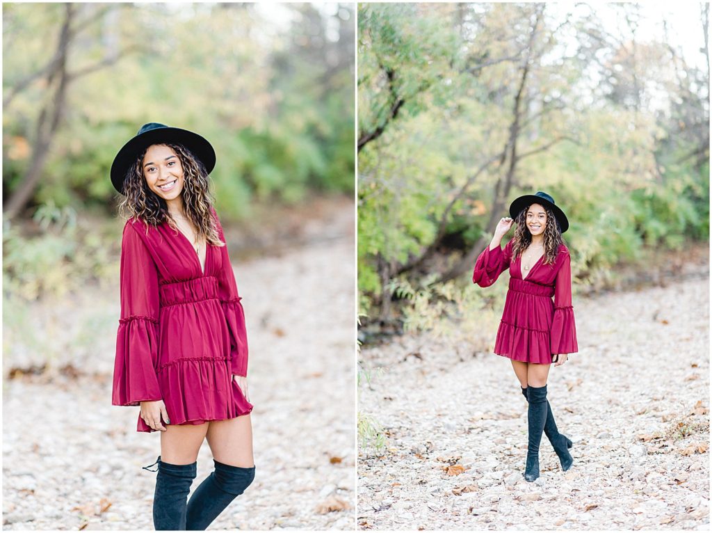 senior girl wearing large black hat and maroon mini dress and tall black boots while posing in creek bed during senior session pictures in Jefferson City, MO