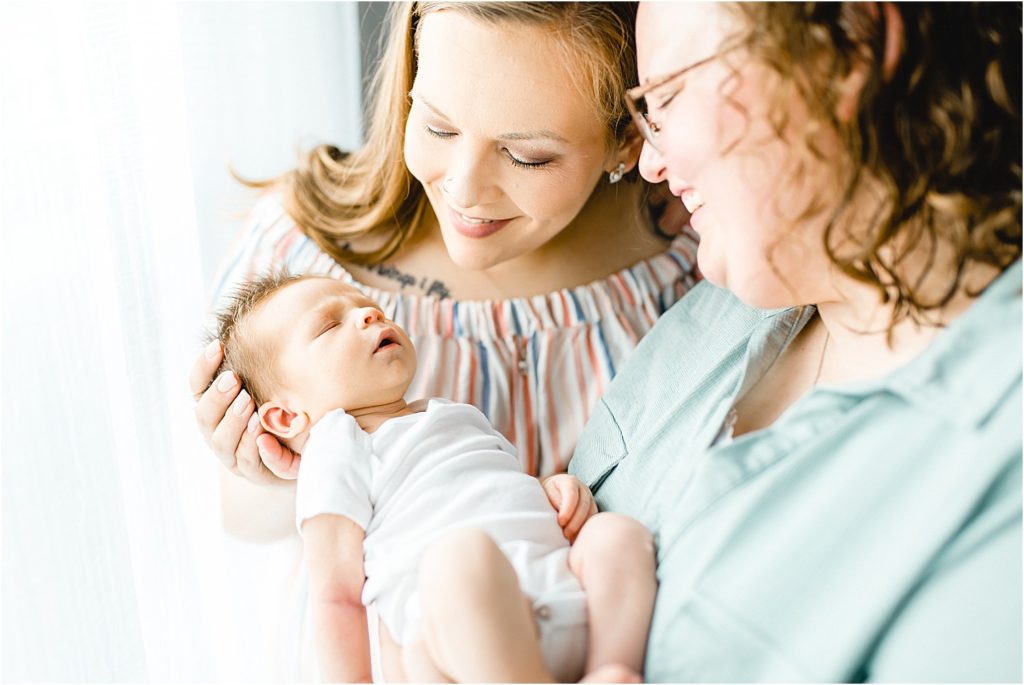 moms smile at baby boy in front of window of natural light studio
