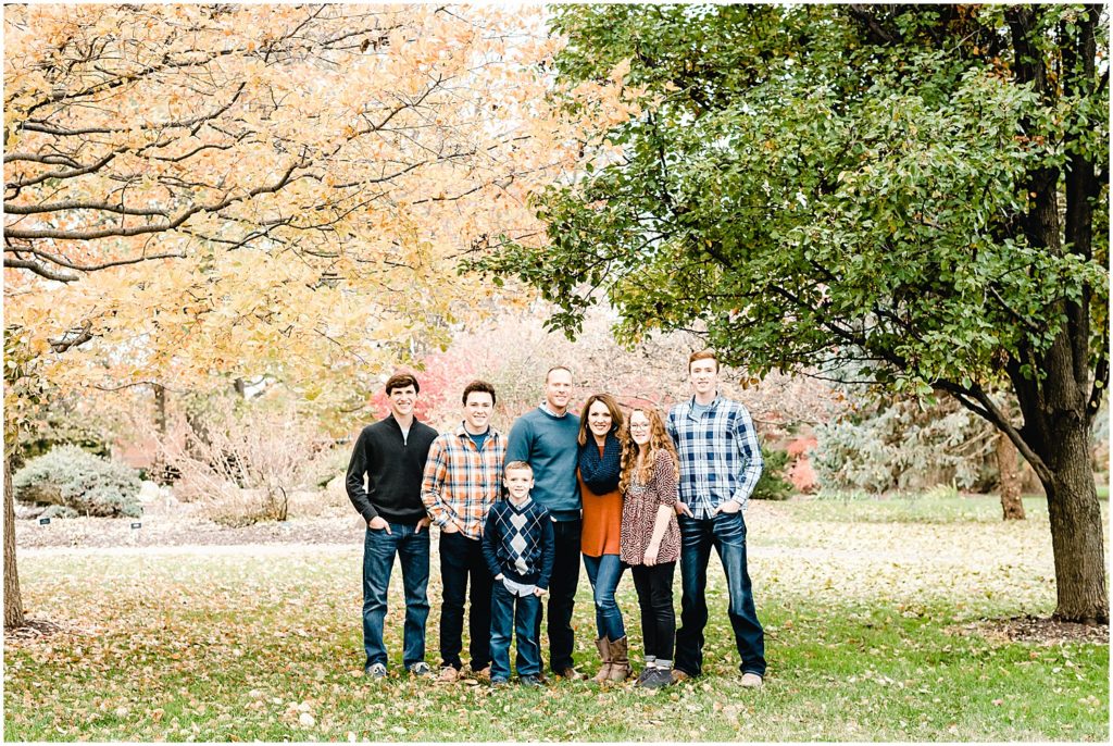 large family in fall clothing standing between two trees with changing colors
