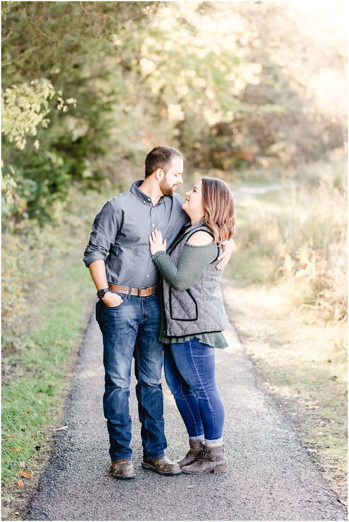 a young engaged couple wearing fall outfits hugging in front of trees