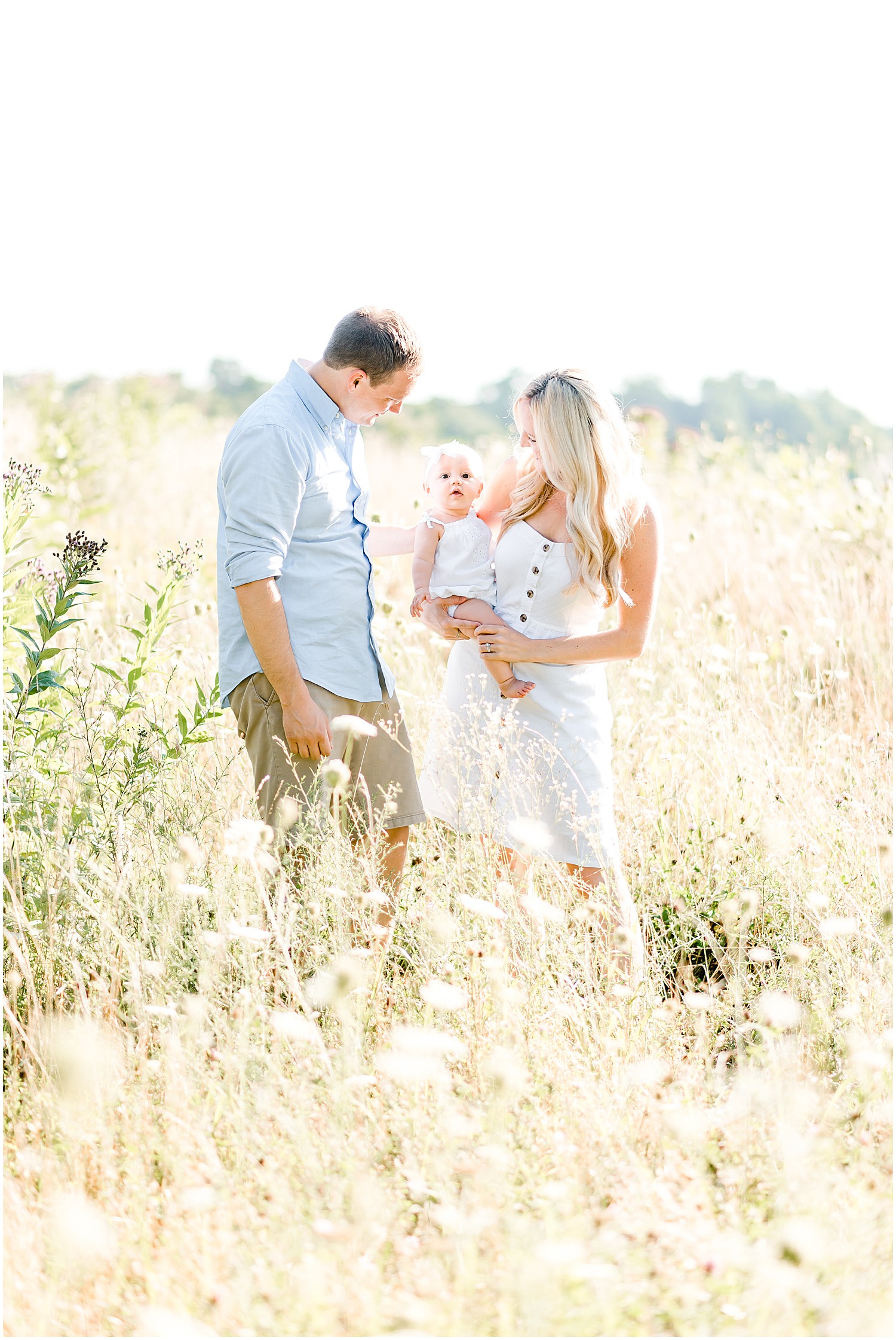 young couple holding baby girl in bright field family portrait session