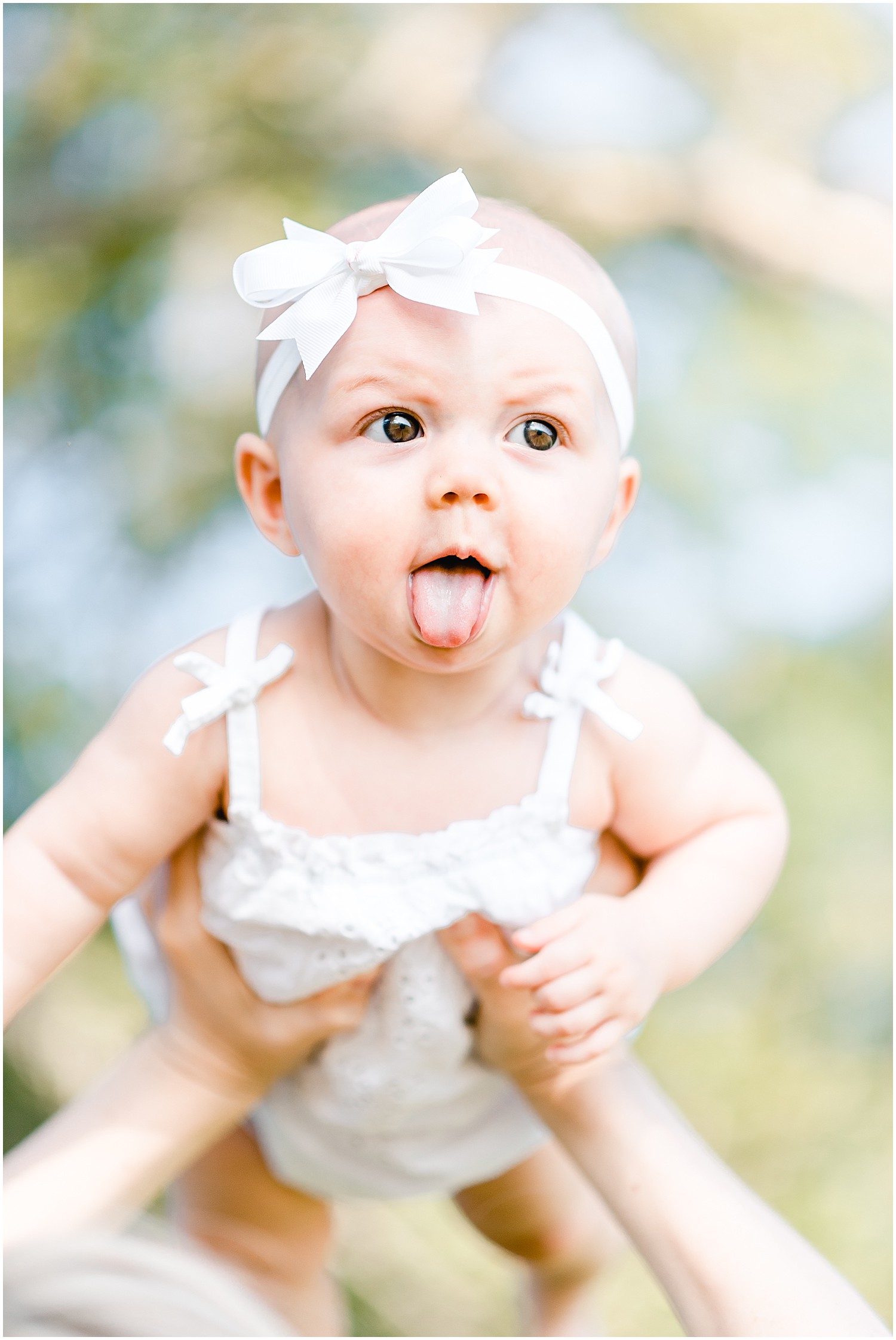 6 month old baby girl being held by mom sticking tongue out family portrait session