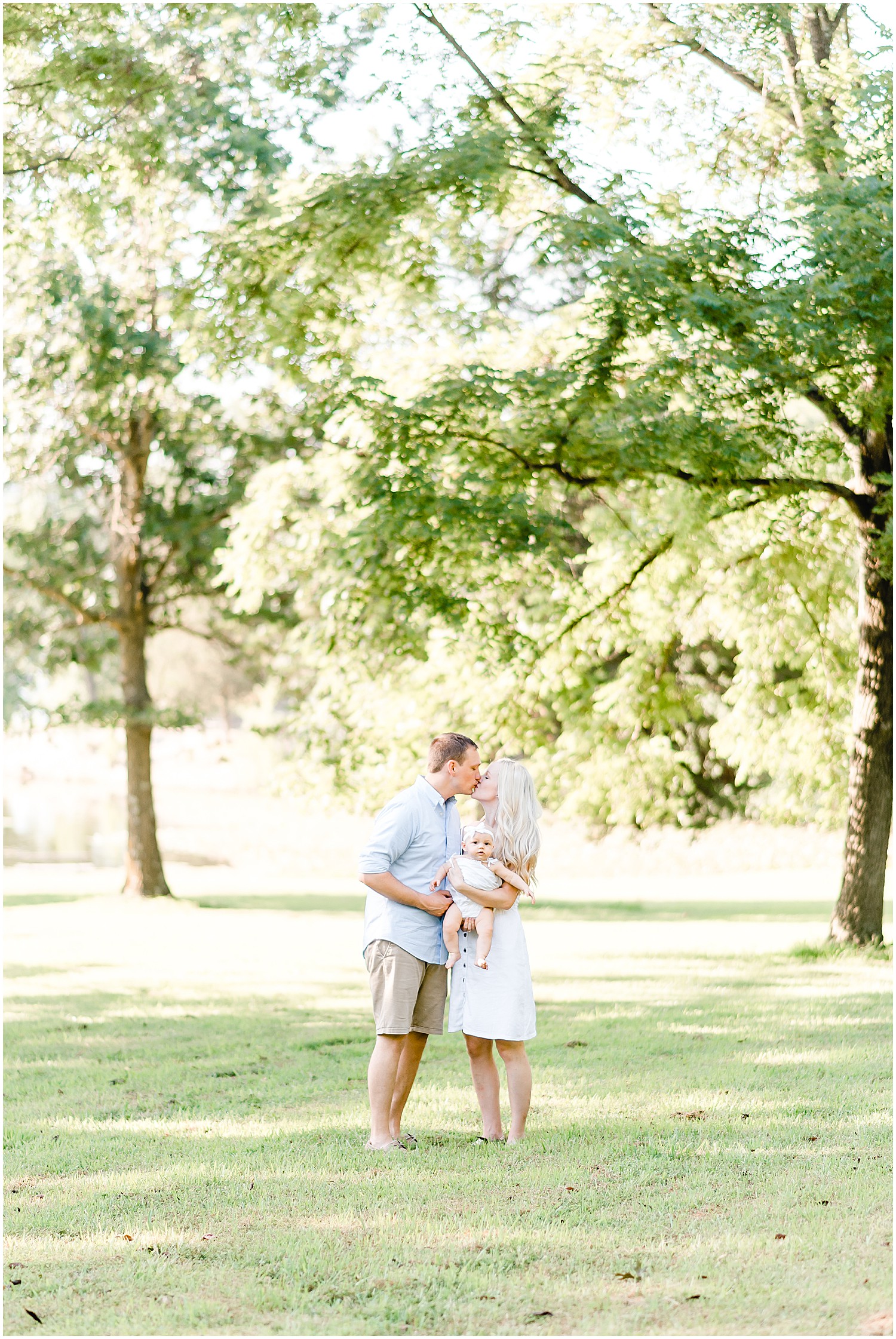 young couple kissing and holding baby girl under trees family portrait session