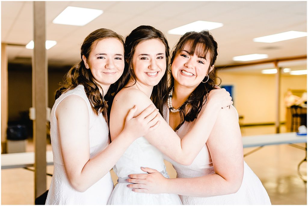 bridesmaids with bride hugging and smiling at camera