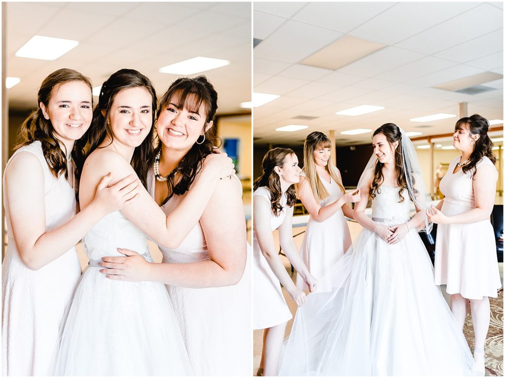 bridesmaids helping bride get into dress and smiling at camera