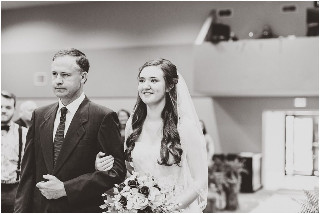 bride walking down aisle with father black and white