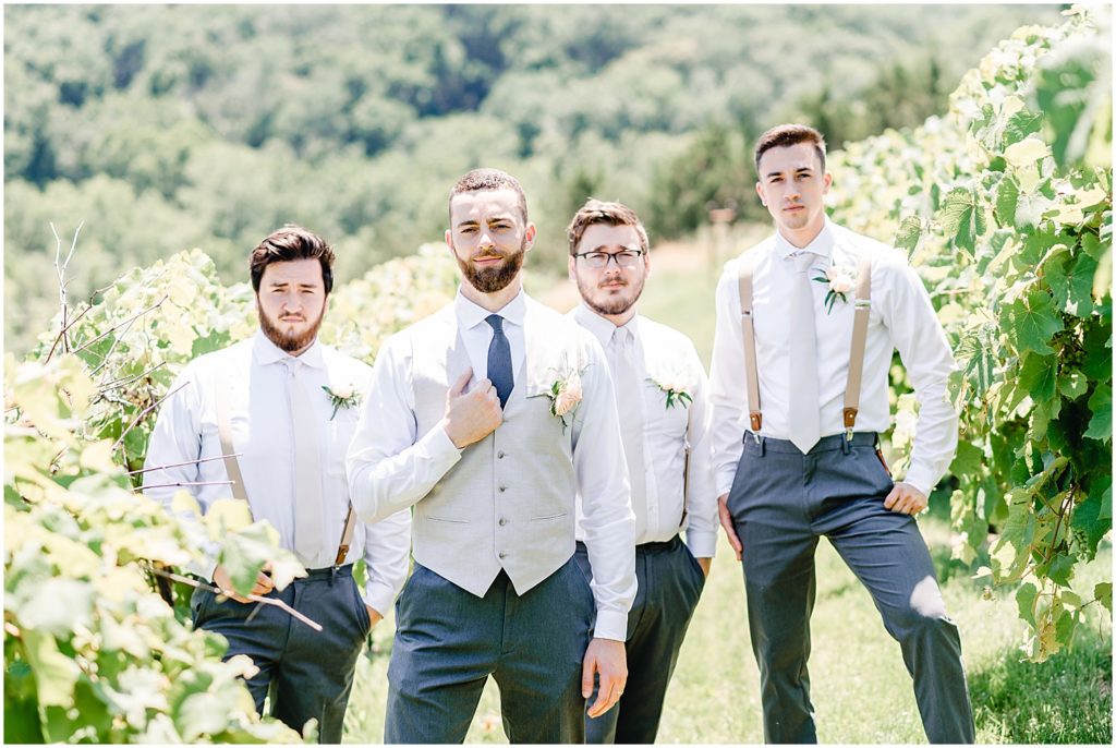 groom and groomsmen standing in vineyard posing