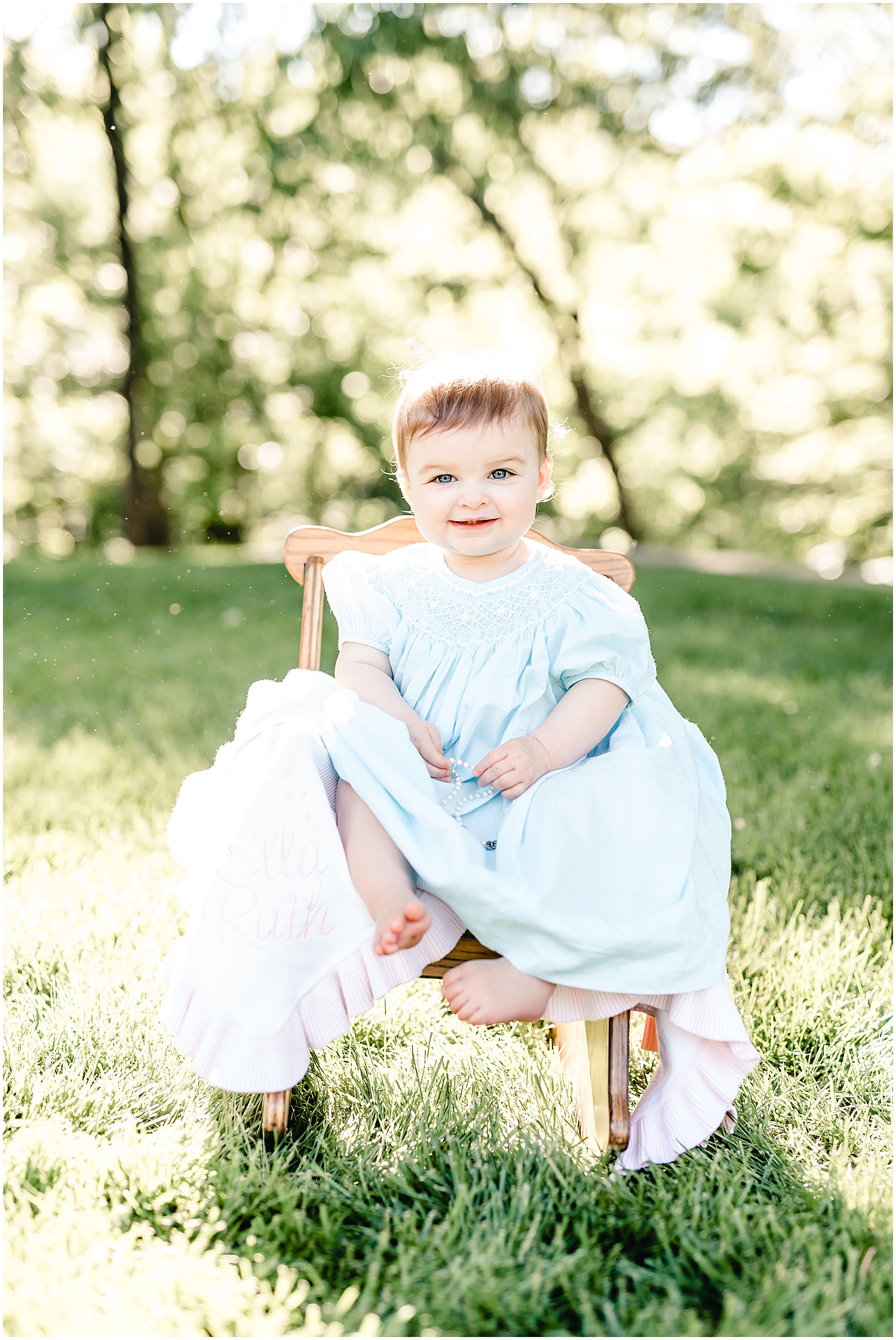 baby girl sitting on chair with blanket on grass sunshine family portrait session