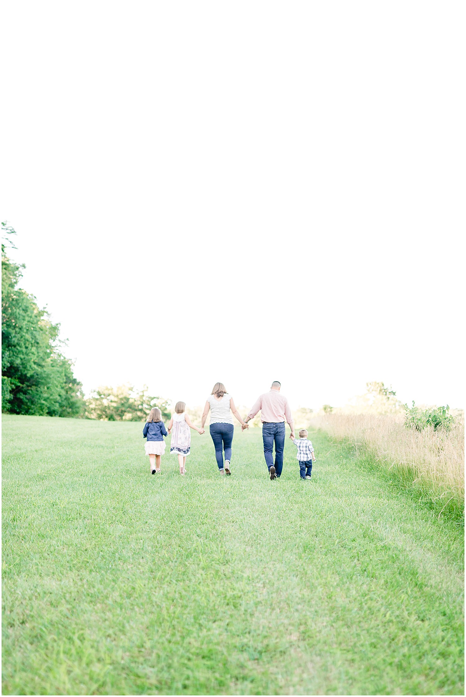 family with three young kids walking in grass away from camera