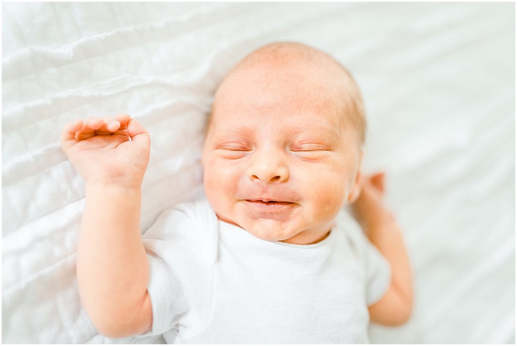 Newborn baby laying on white bed smiling