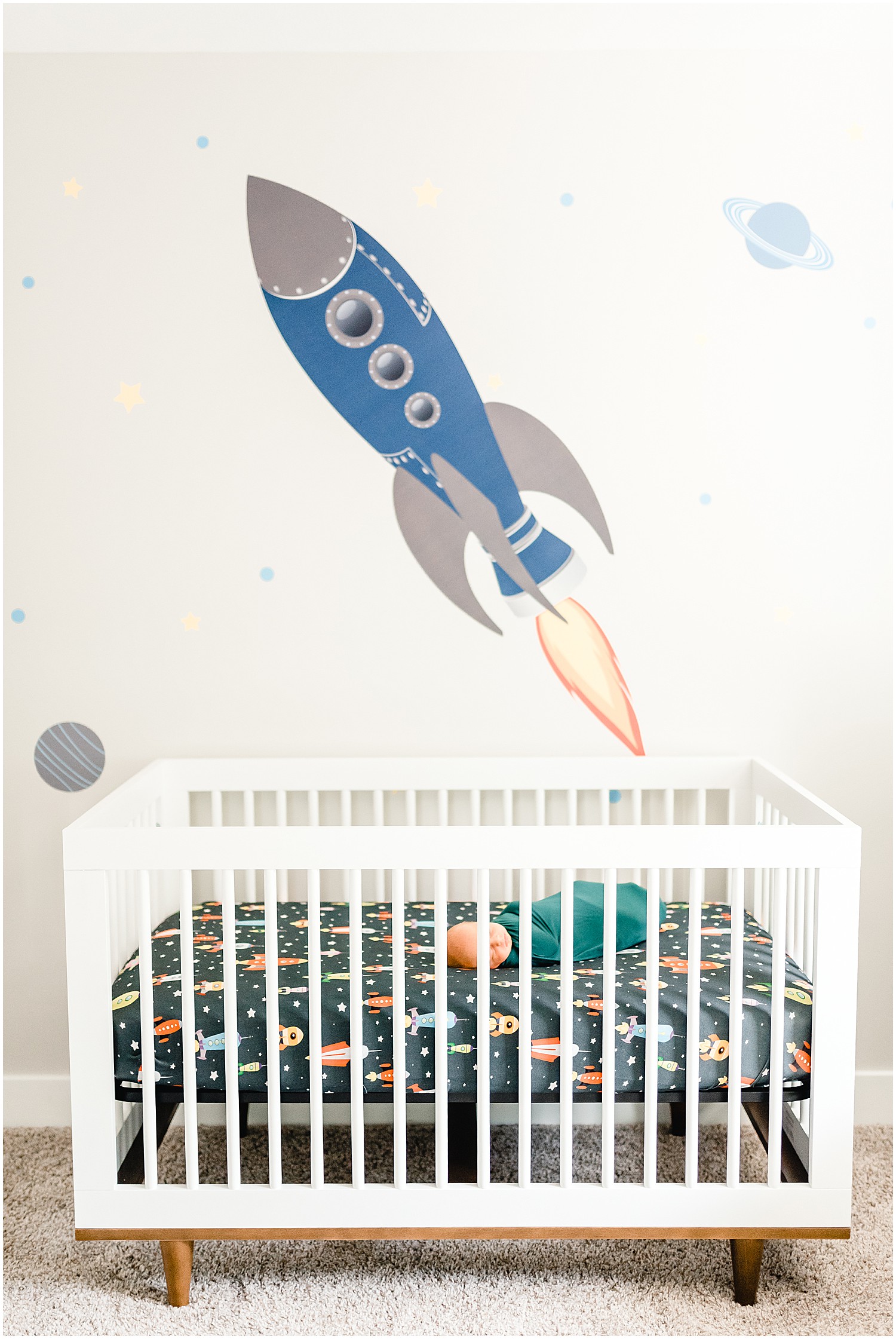 newborn baby in crib with rocket space theme nursery decoration