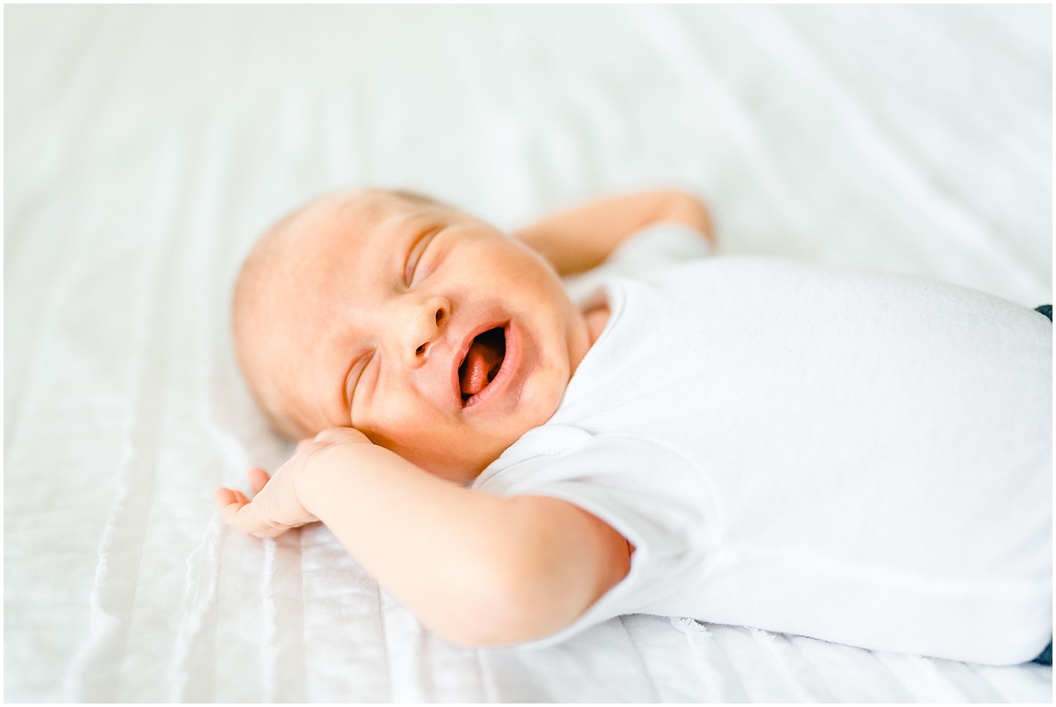 Newborn smiling on white bed newborn session