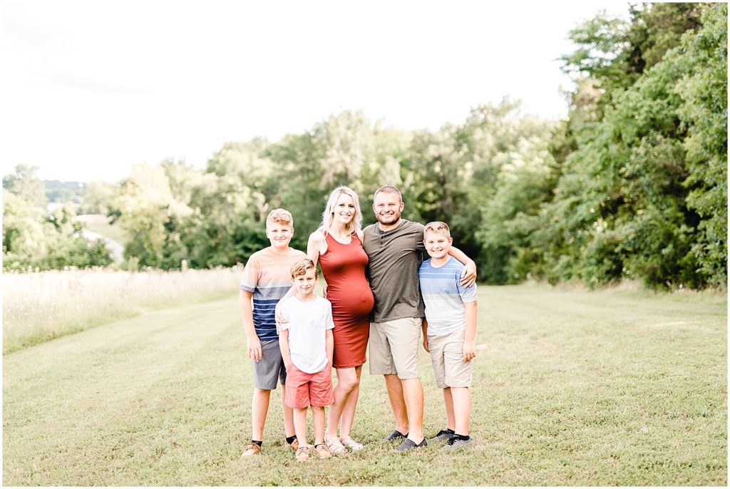 Family with pregnant mom in red dress smiling at camera