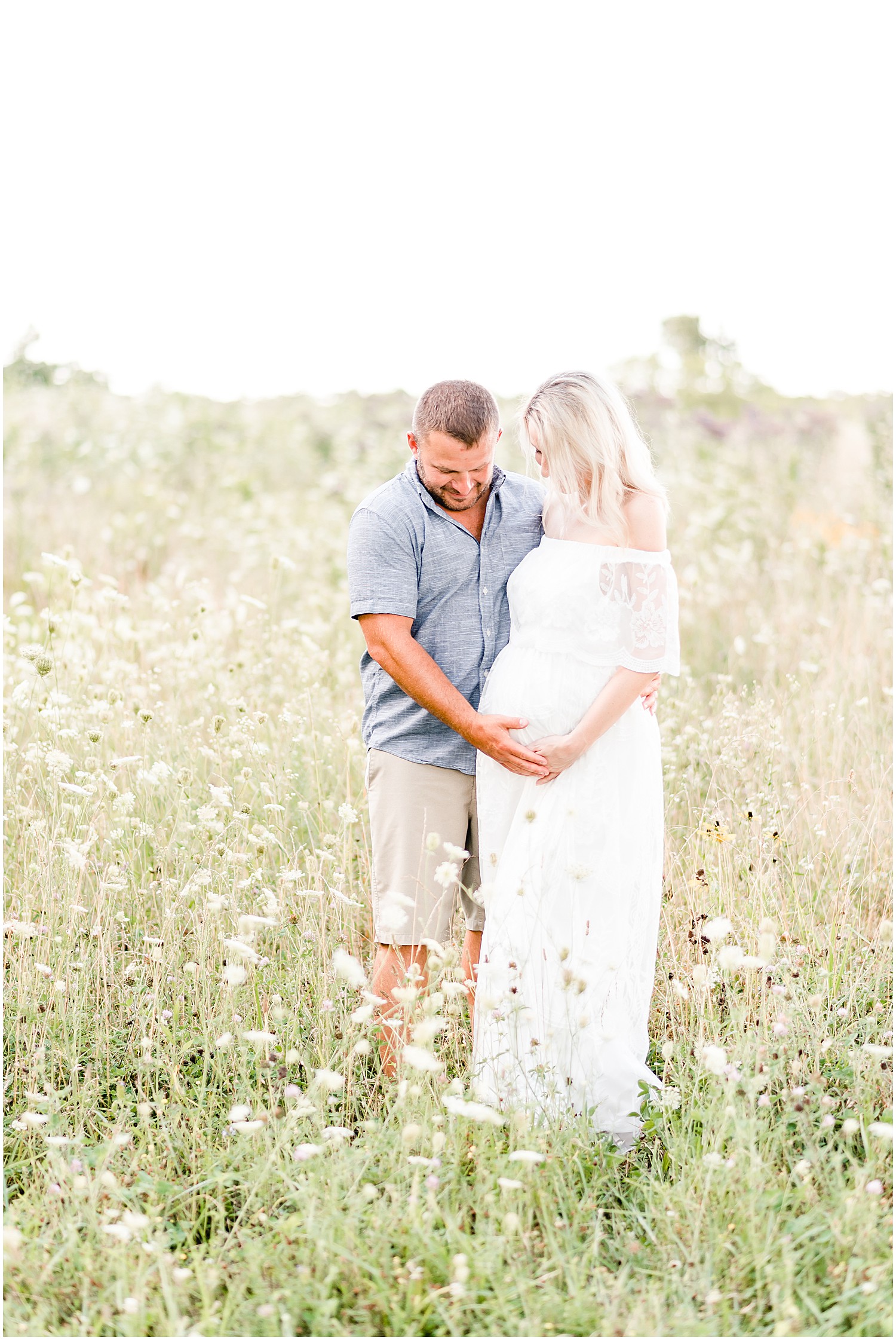 pregnant mom and dad long white dress standing in wildflower field