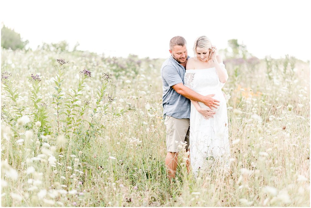 pregnant mom and dad touching belly in wildflower field