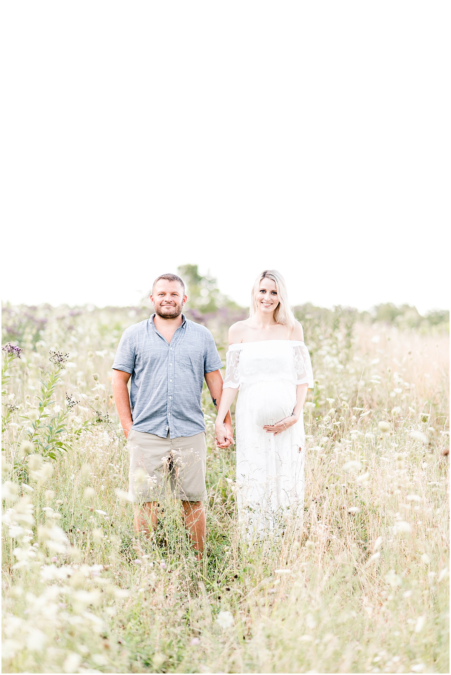 pregnant mom and dad standing in wildflower field holding hands