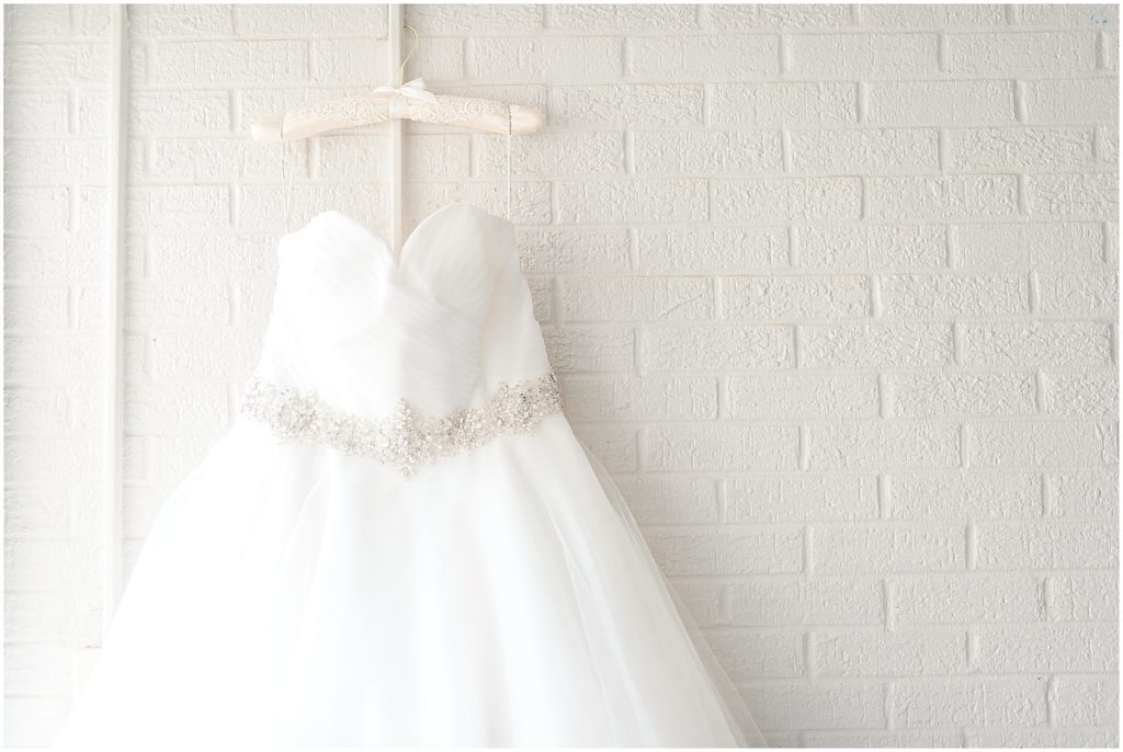white wedding dress hanging on white brick church wall