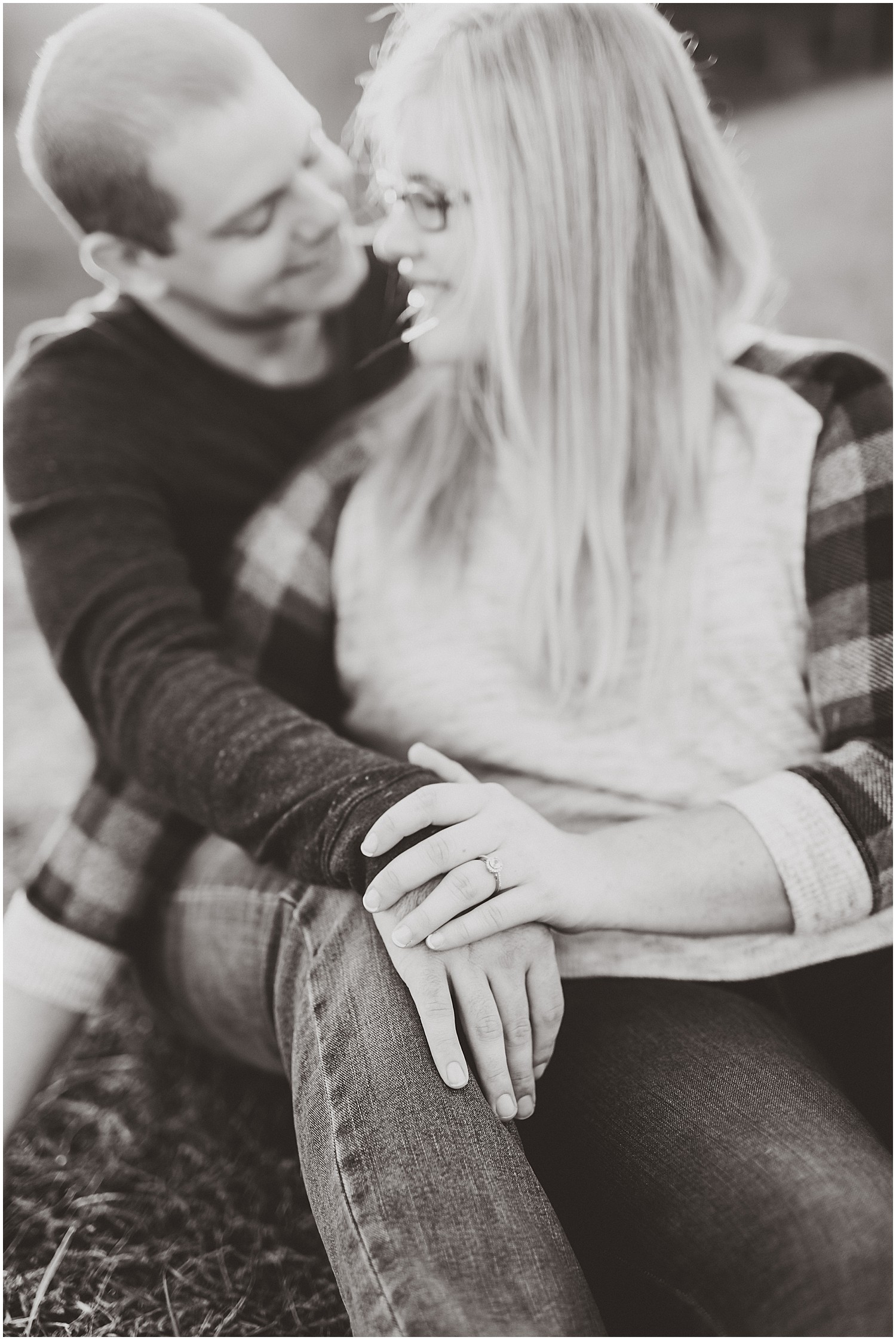 couple sitting together showing rings holding hands black and white engagement session