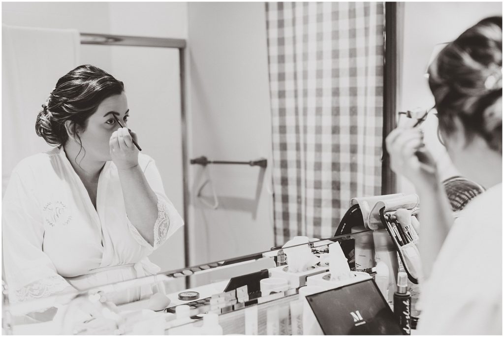 bride doing makeup in mirror black and white