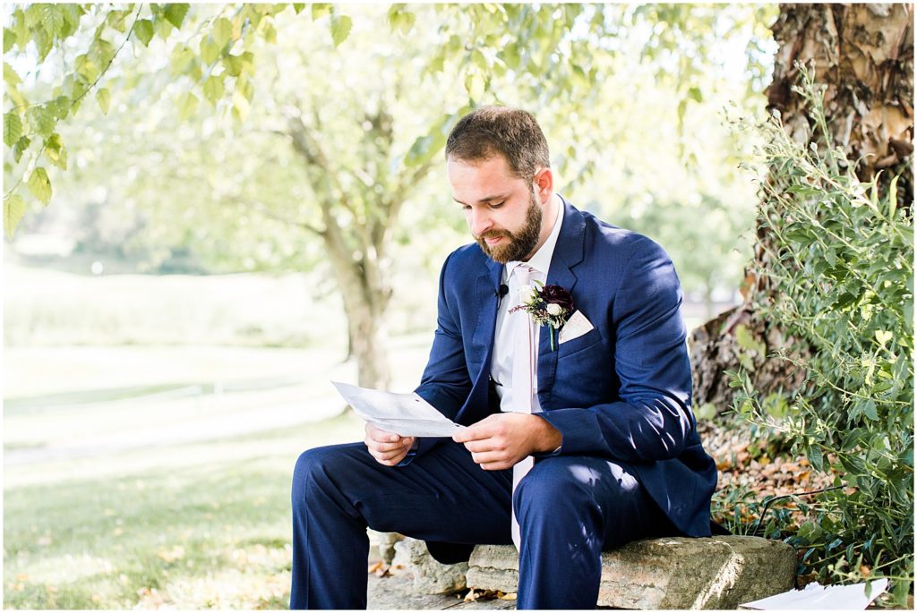 groom reading letter sitting under tree Old Kinderhook wedding