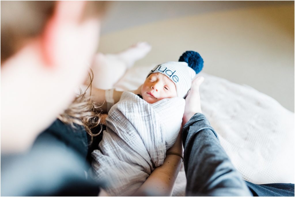 newborn baby laying in dads arms looking at dad blue hat on
