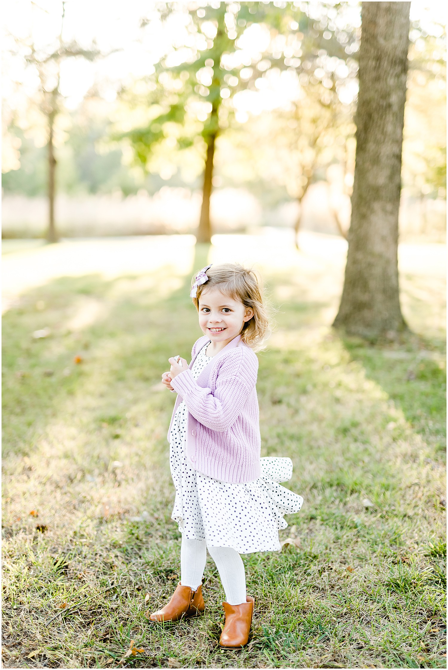 little girl spinning in dress smiling under trees sunlight