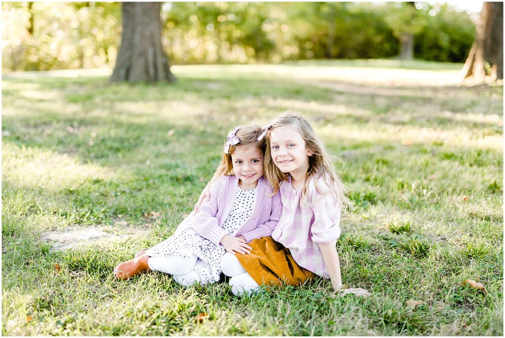 two little girls sitting on grass posing smiling hugging