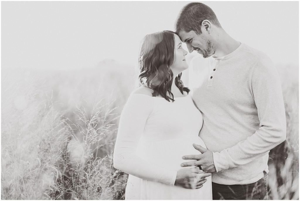 black and white couple standing in field holding baby belly foreheads touching
