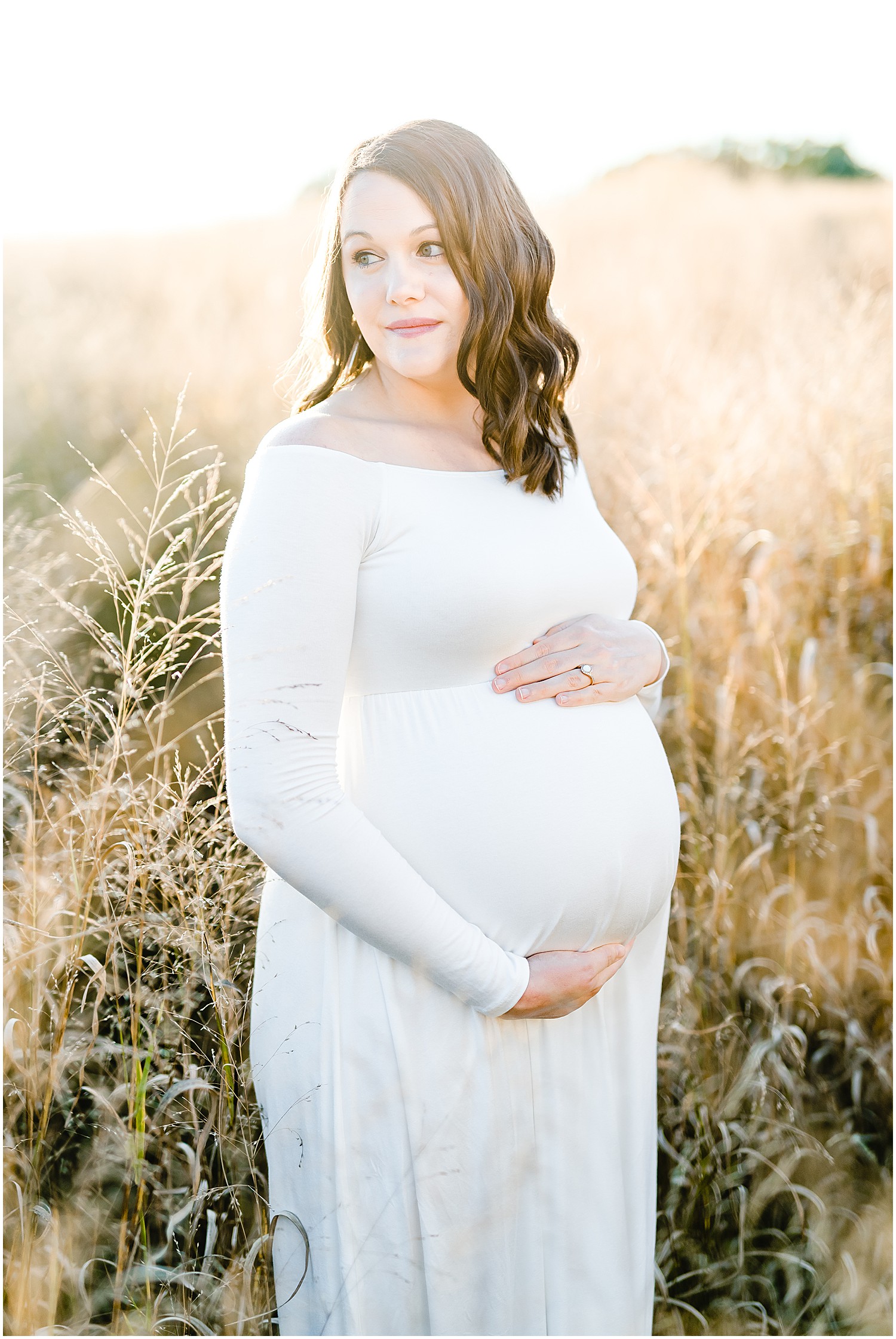 expecting mom white maternity dress in tall grass holding baby belly