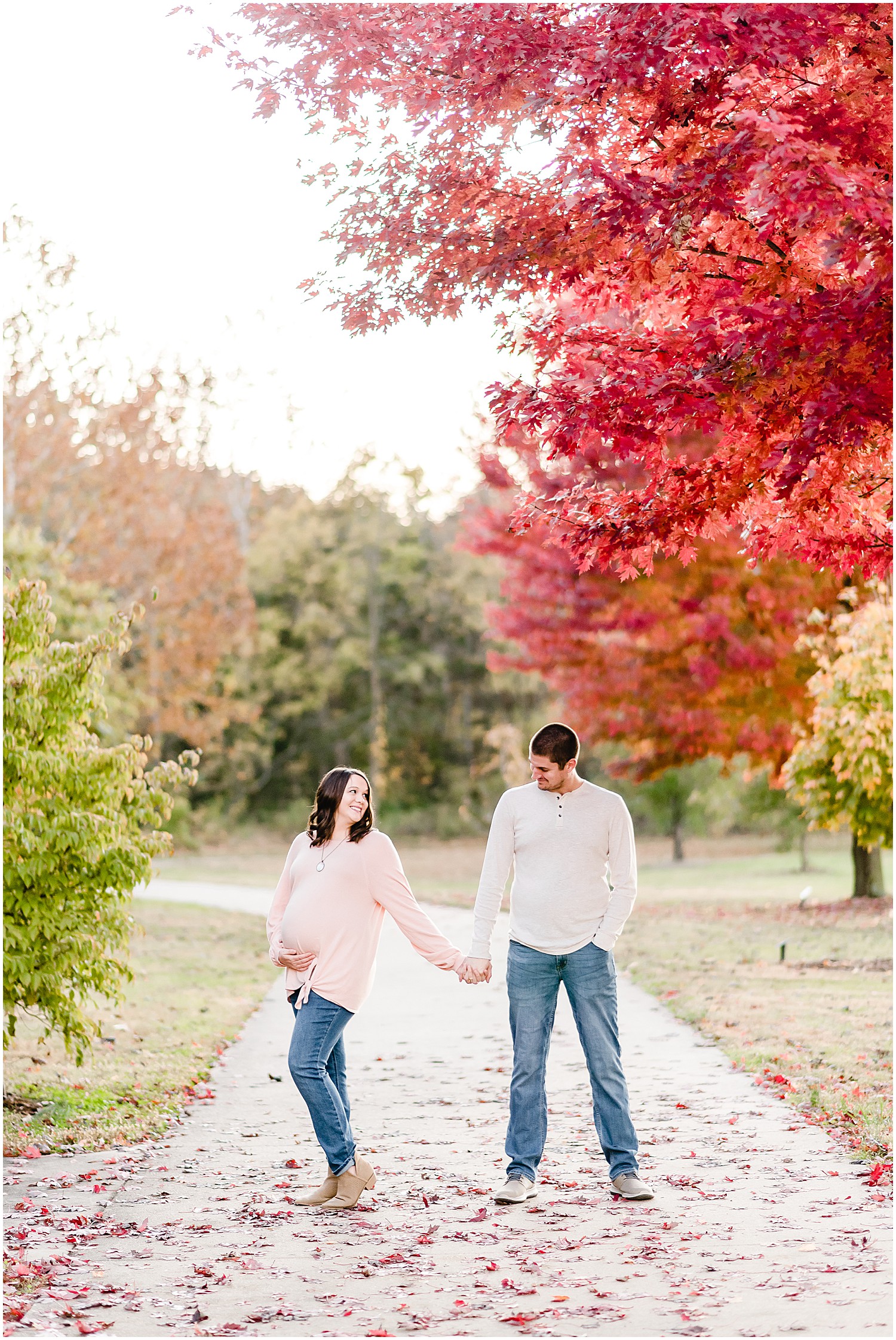 expecting couple under bright trees holding baby belly