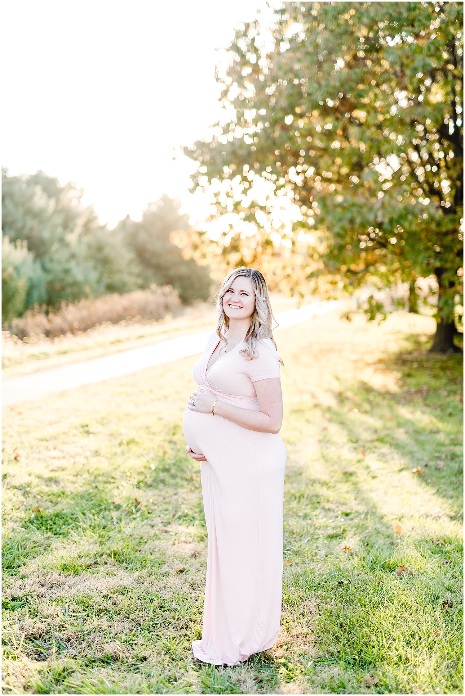 expecting mom standing in sunlight in front of tree long pink dress st Joseph mo maternity session