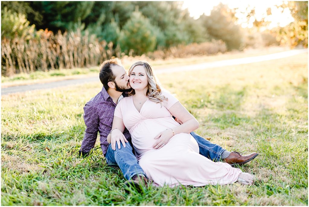 couple sitting on grass sunlight maternity session