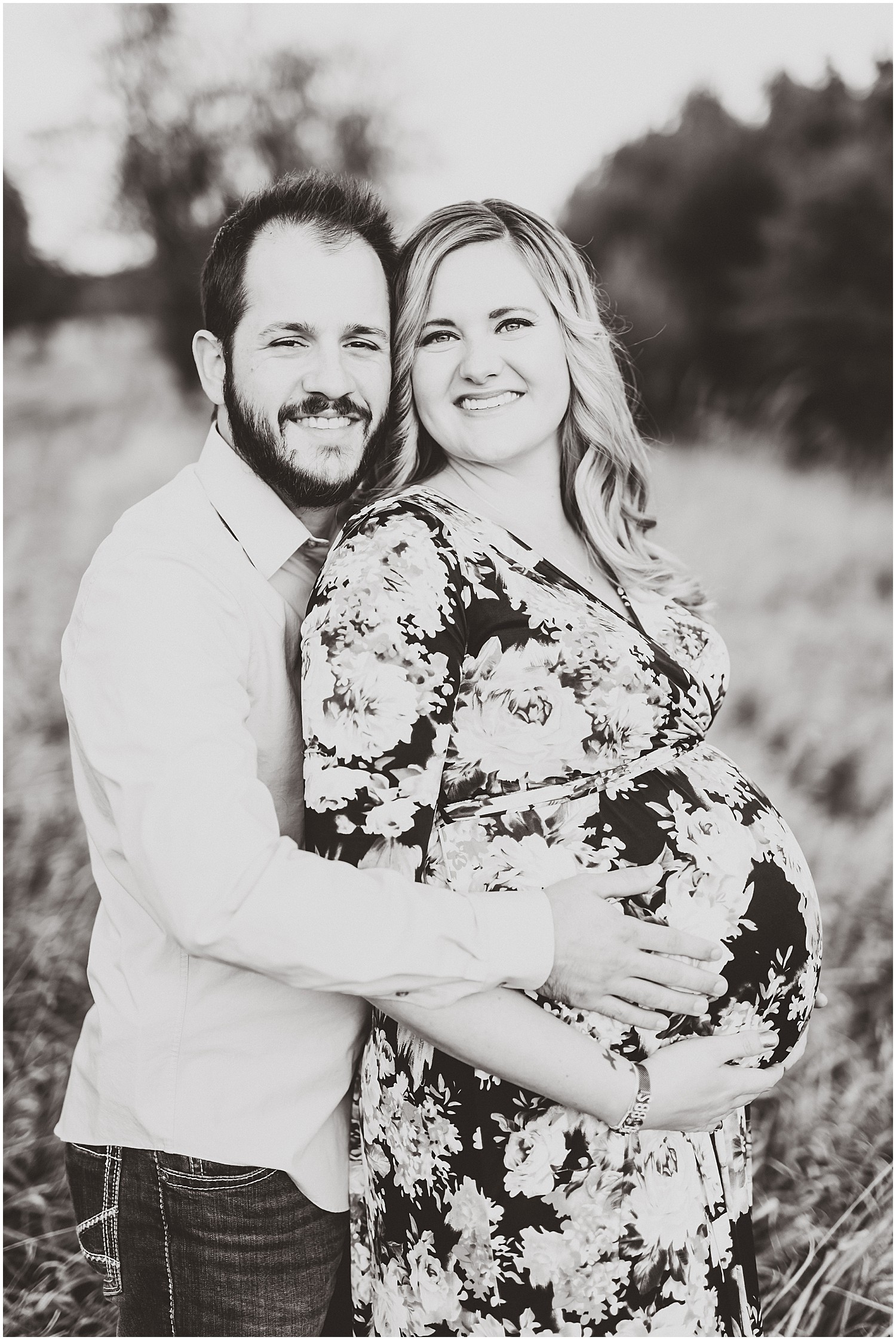 black and white expecting couple smiling at camera holding baby belly maternity session