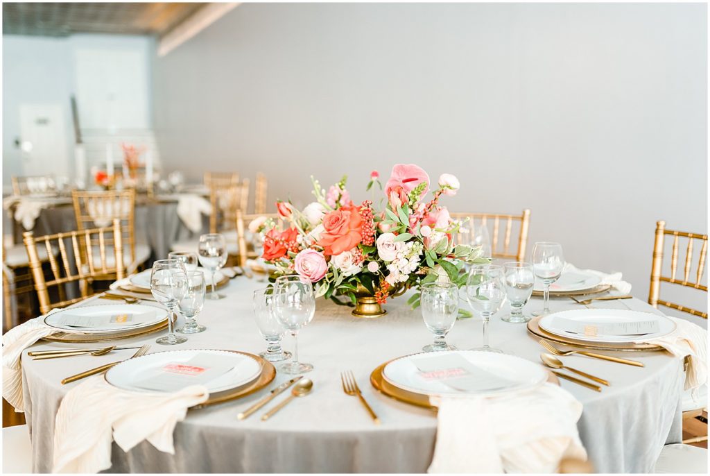table setting with large pink and coral centerpiece and gold accents