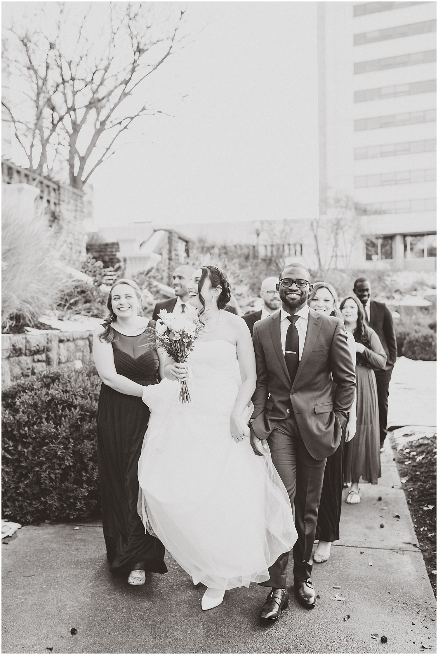 bride and groom walking with wedding party black and white