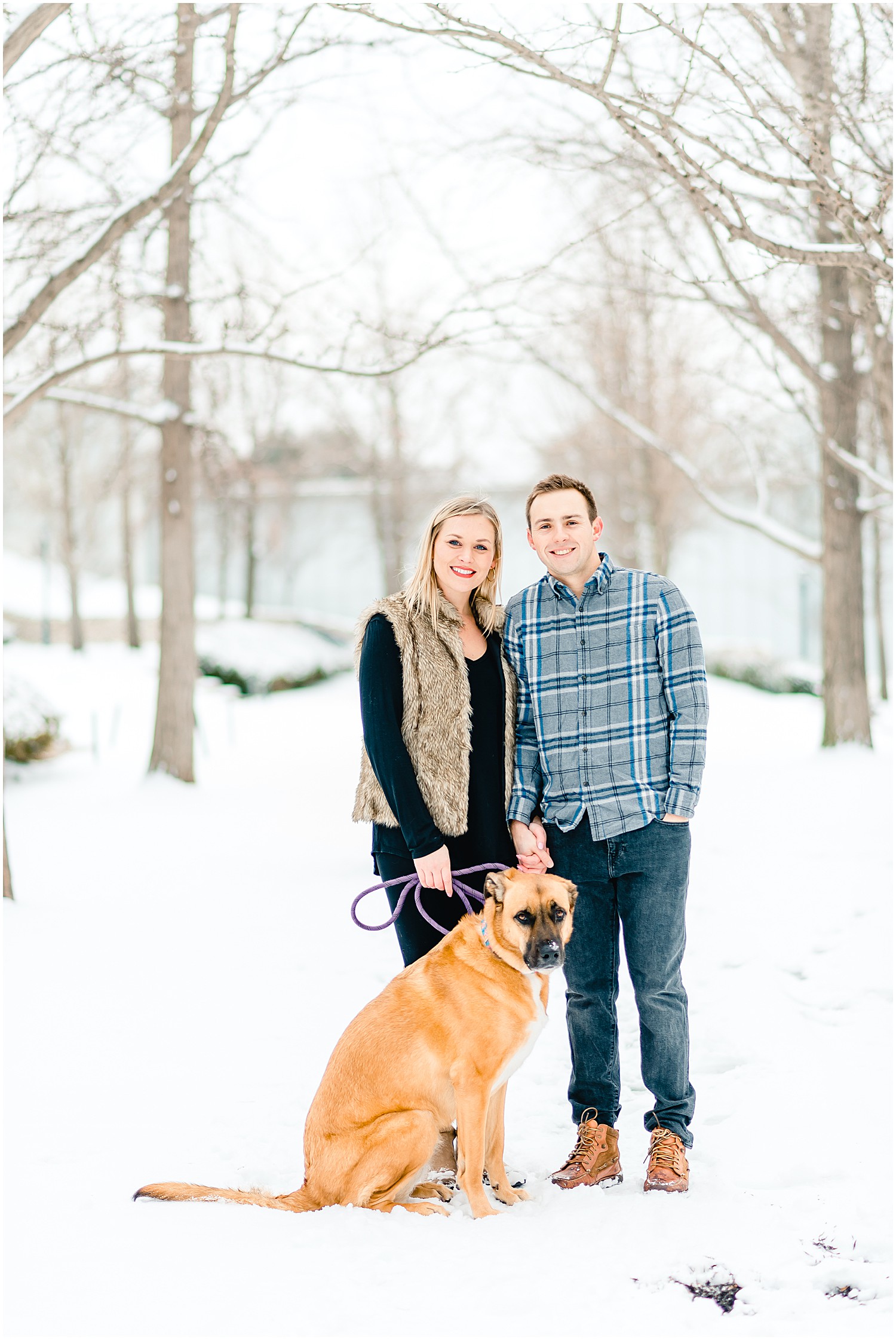 couple standing in snow with dog winter engagement session
