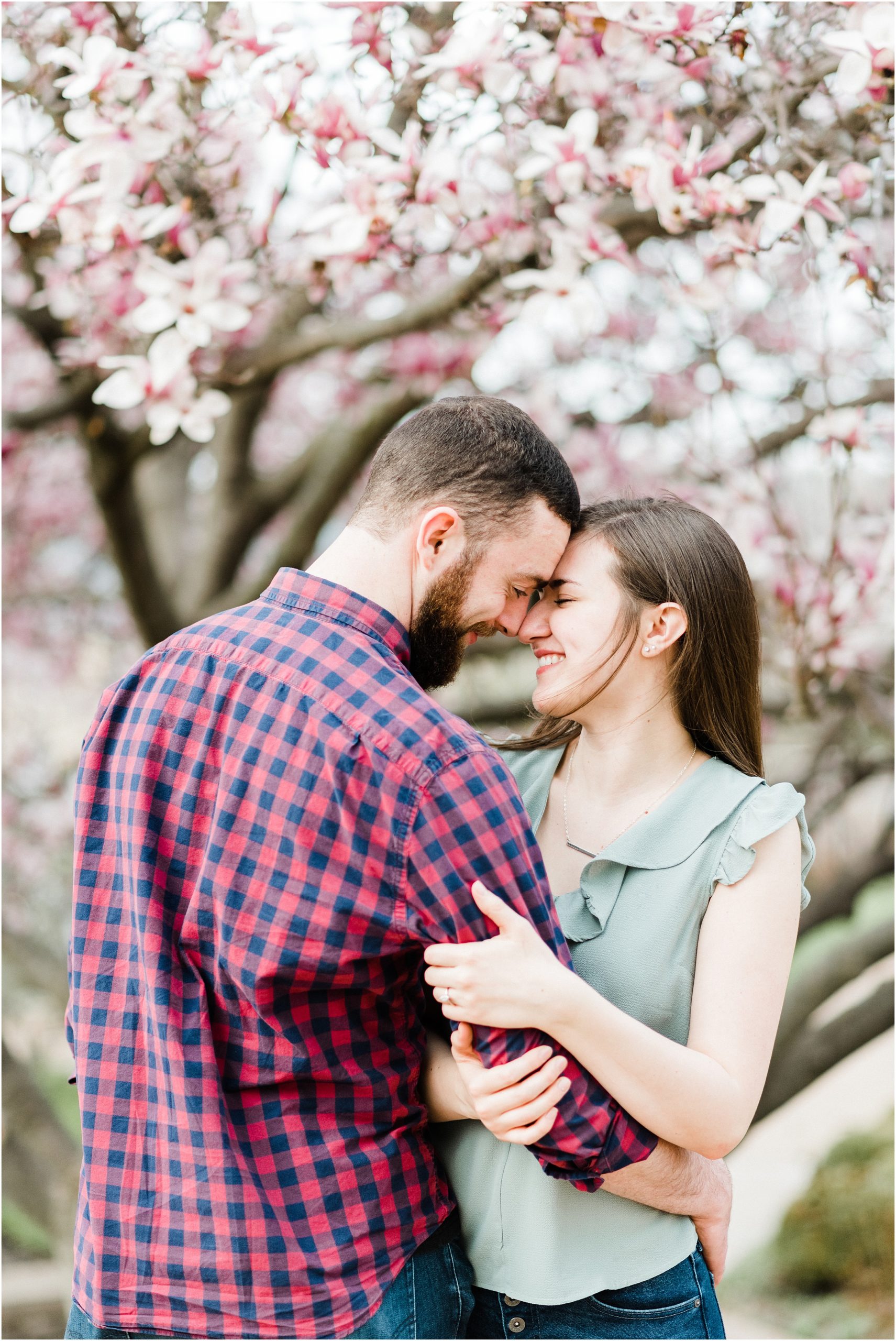 Engaged couples poses in front of magnolia tree for engagement session