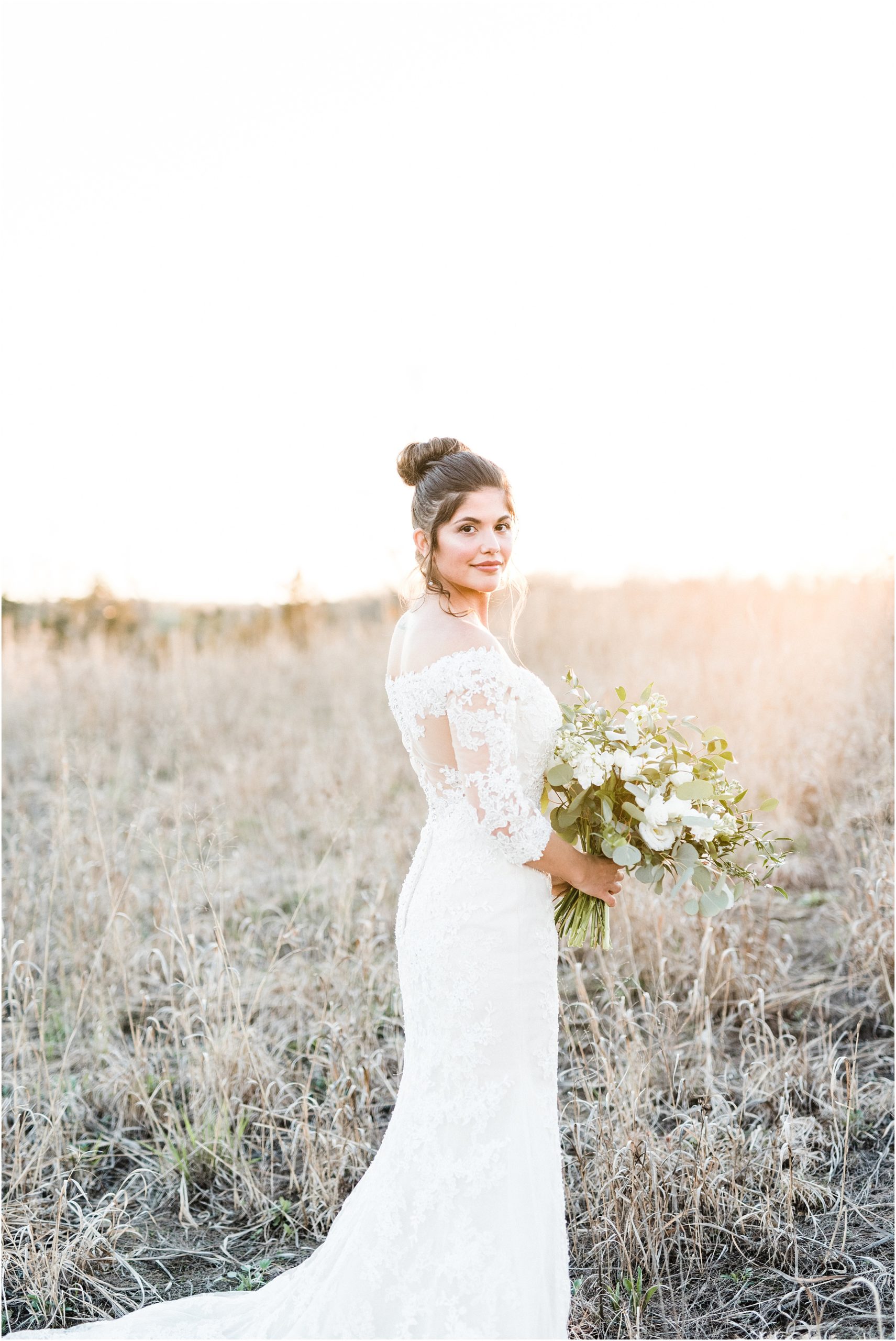 bride looking over shoulder during bridal session with sunset in background in field