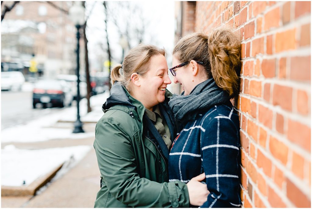 female couple smiling against brick wall