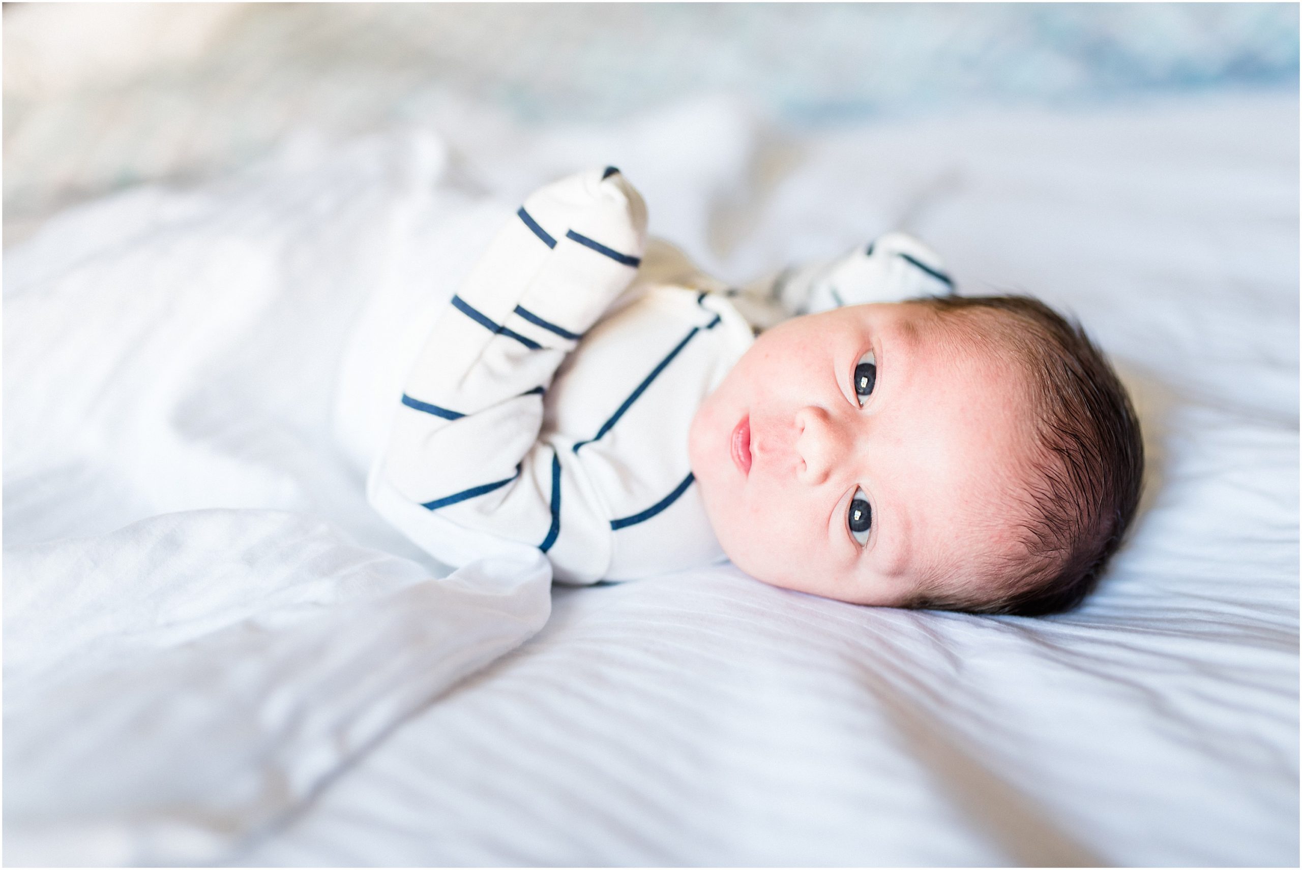 newborn baby boy laying on white sheets for newborn session in home