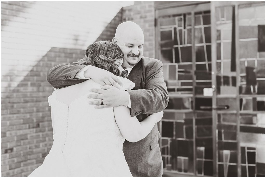 bride and dad hugging outside of chapel after first look in black and white
