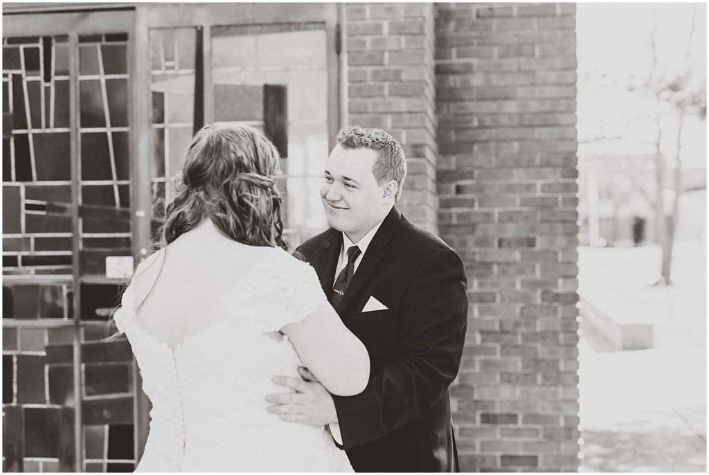 groom smiling at bride outside of chapel in black and white