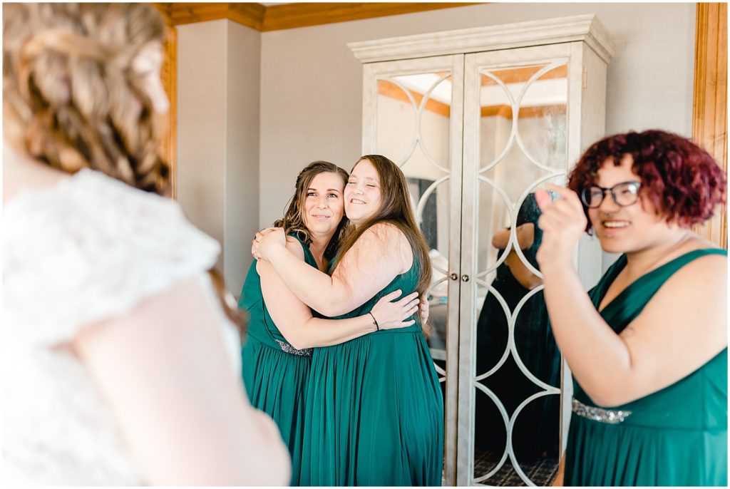 bridesmaids hugging while looking at bride getting in wedding gown